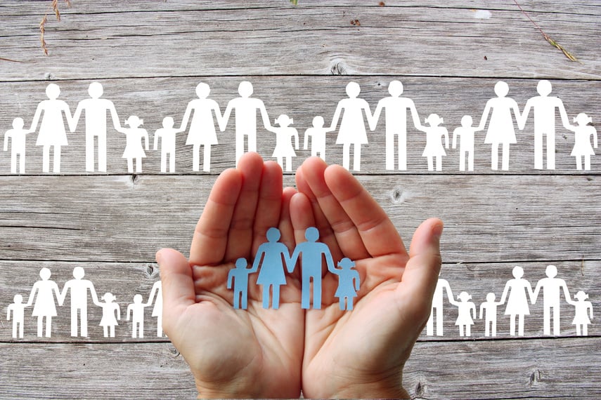 Paper family in hands on wooden background with white families